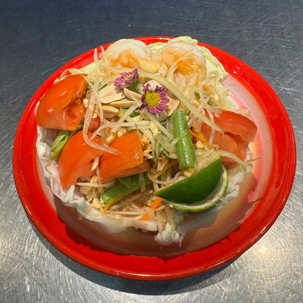 Som Tum, a Thai papaya salad with shrimp, tomatoes, green beans, peanuts, and lime on a red plate.