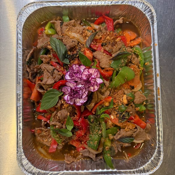 Spicy beef stir-fry with bell peppers, basil, and a purple flower garnish in a foil container.