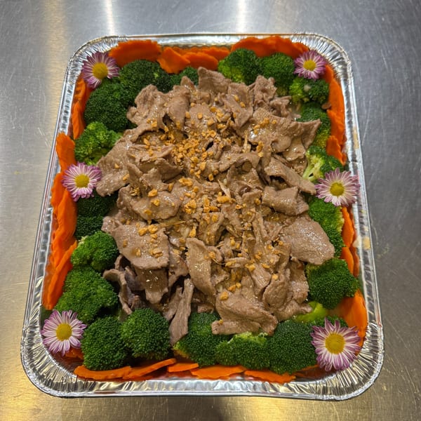 Beef with broccoli and carrots, garnished with flowers, in a foil tray on a metal surface.